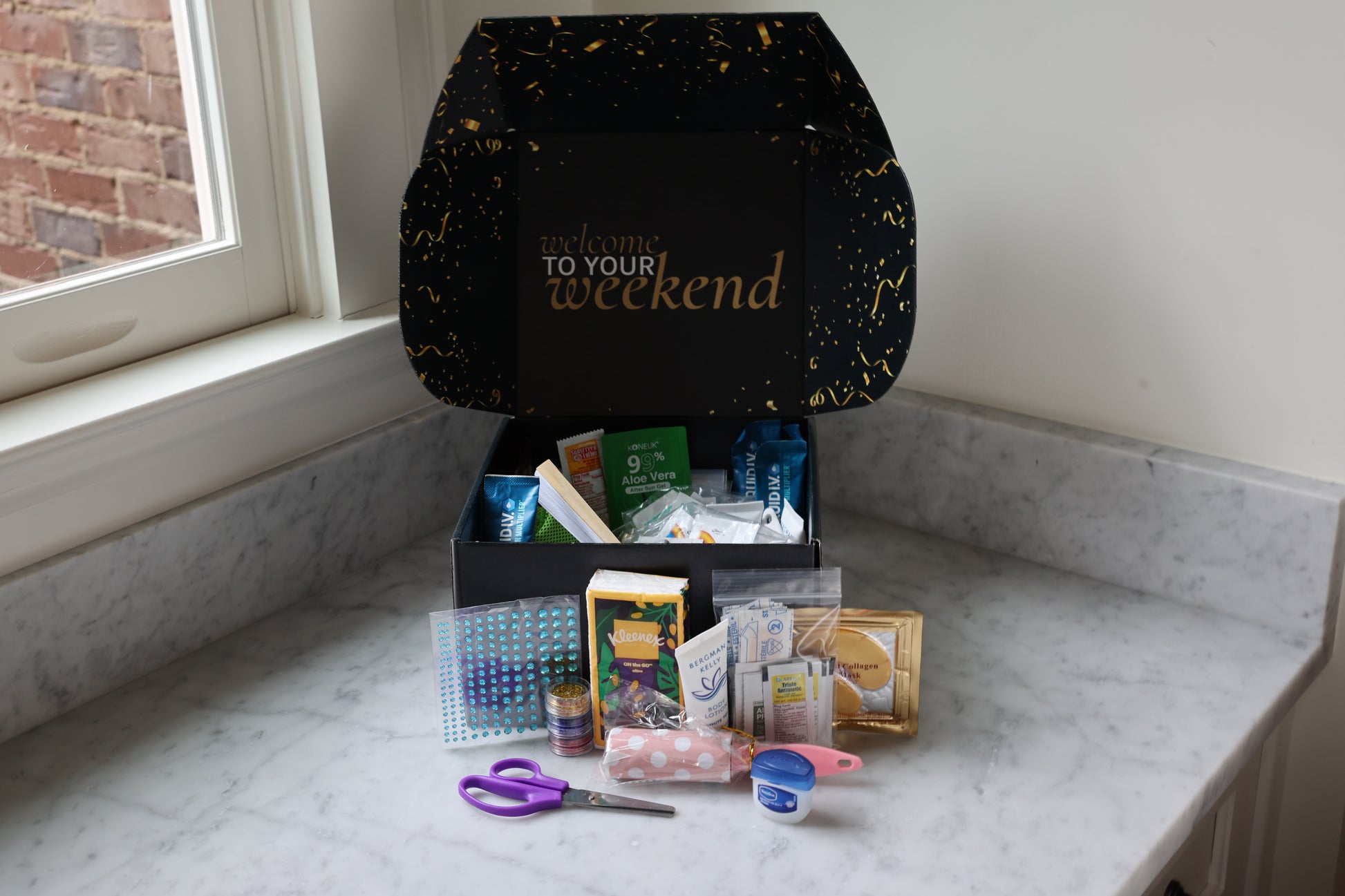 Black box labeled 'Welcome To Your Weekend' on a marble surface with various items spilling out.
